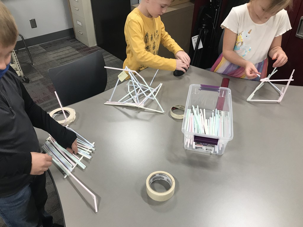 Three students building straw towers