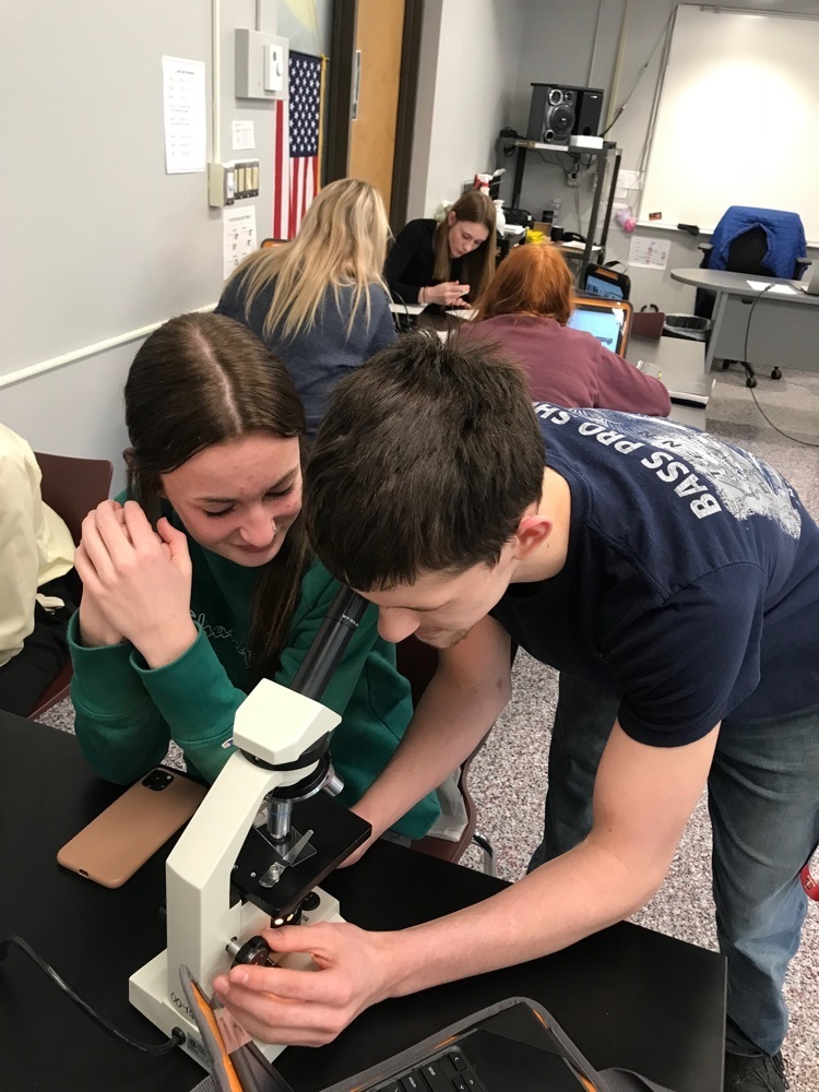 Cam Manecke helping Sienna Friesen find a microorganism on a light microscope. 